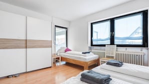 A modern bedroom with a wooden floor, a bed with white bedding, a window with a view, and a radiator.