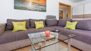 A living room with a sofa, a glass coffee table, and a painting of a sunset over the ocean.