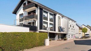 A modern two-story building with a balcony, a garage, and a solar panel on the roof.