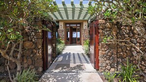 A pathway leading to a building with a green pergola, stone walls, and a wooden door. - Wai'ula'ula Villa 409 Four Bedroom (Kohala Coast)