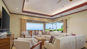 A spacious living area with a large sofa, a coffee table, and a TV on a wooden cabinet. - Wai'ula'ula Villa 409 Four Bedroom (Kohala Coast)