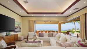 A spacious living room with a large flat-screen TV, comfortable seating, and a view of the ocean. - Wai'ula'ula Villa 409 Four Bedroom (Kohala Coast)