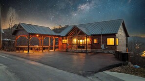 Eine Lodge mit überdachter Außenbestuhlung, Steinmauern und sternenklarer Nacht.