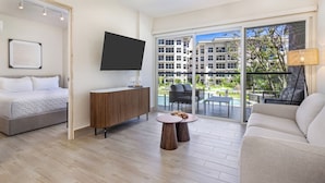 Una habitación de hotel moderna con una cama, un televisor, un armario de madera, una mesa redonda y un sofá.