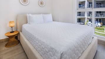 A modern bedroom with a large bed, a bedside lamp, and a view of a building with balconies.