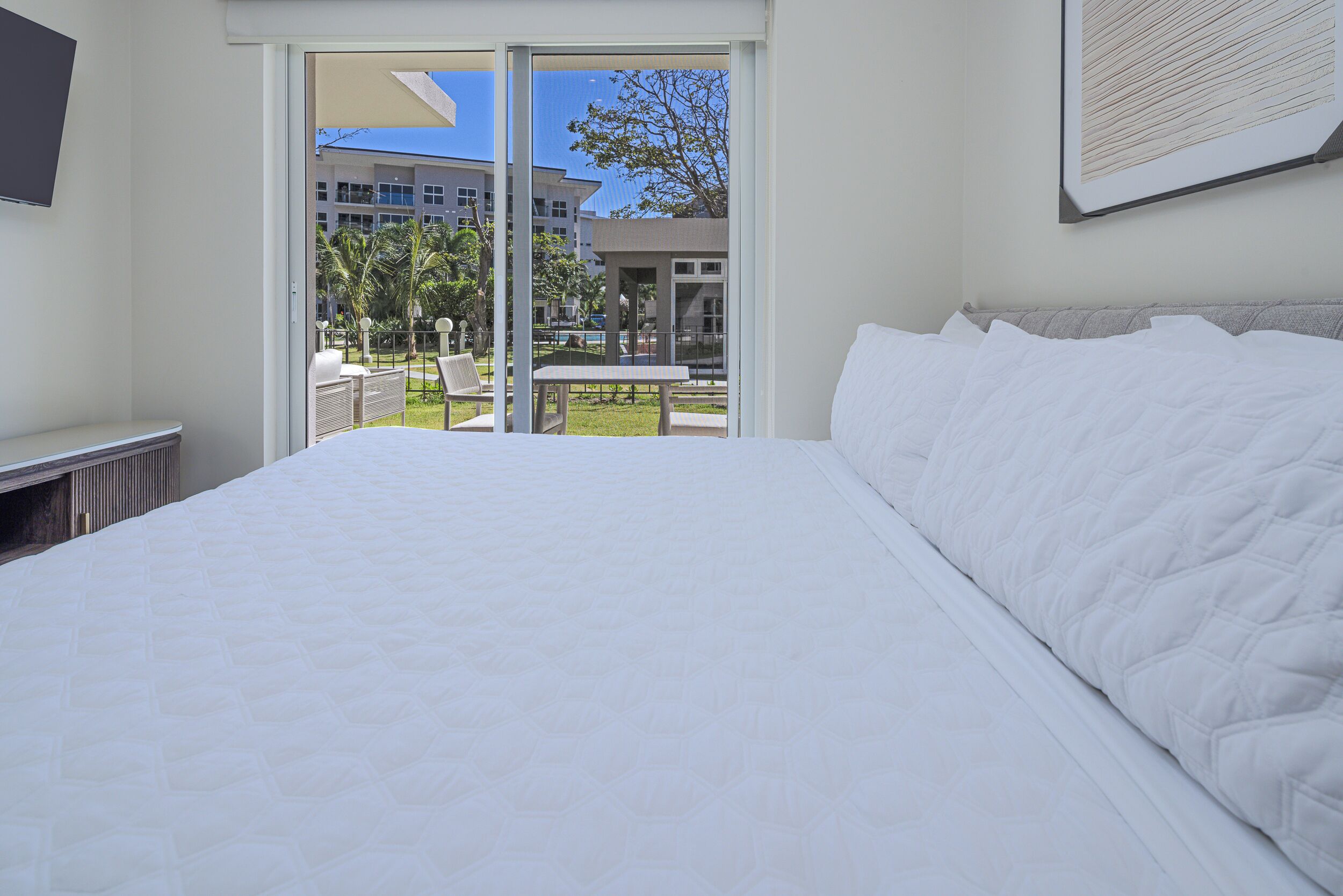 Camera d'albergo con un letto grande, una porta scorrevole in vetro che dà su un balcone con mobili da esterno e vista sugli edifici.