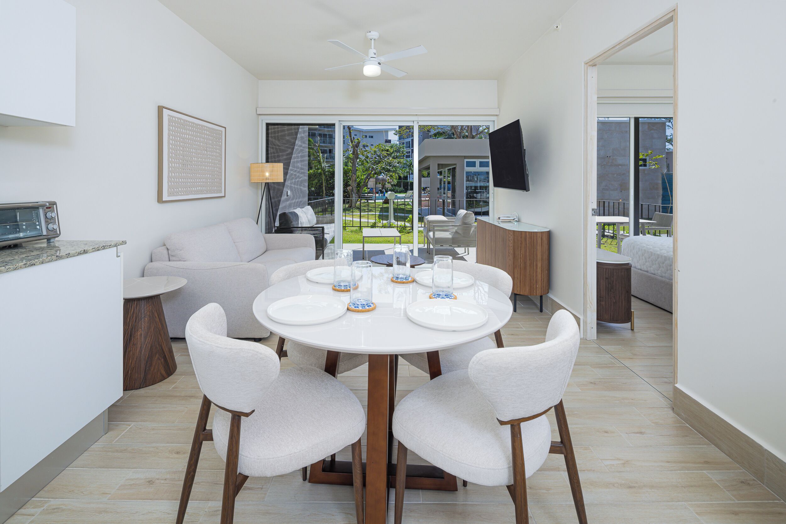 A modern dining area with a round table, white chairs, and a view of a balcony with outdoor furniture.