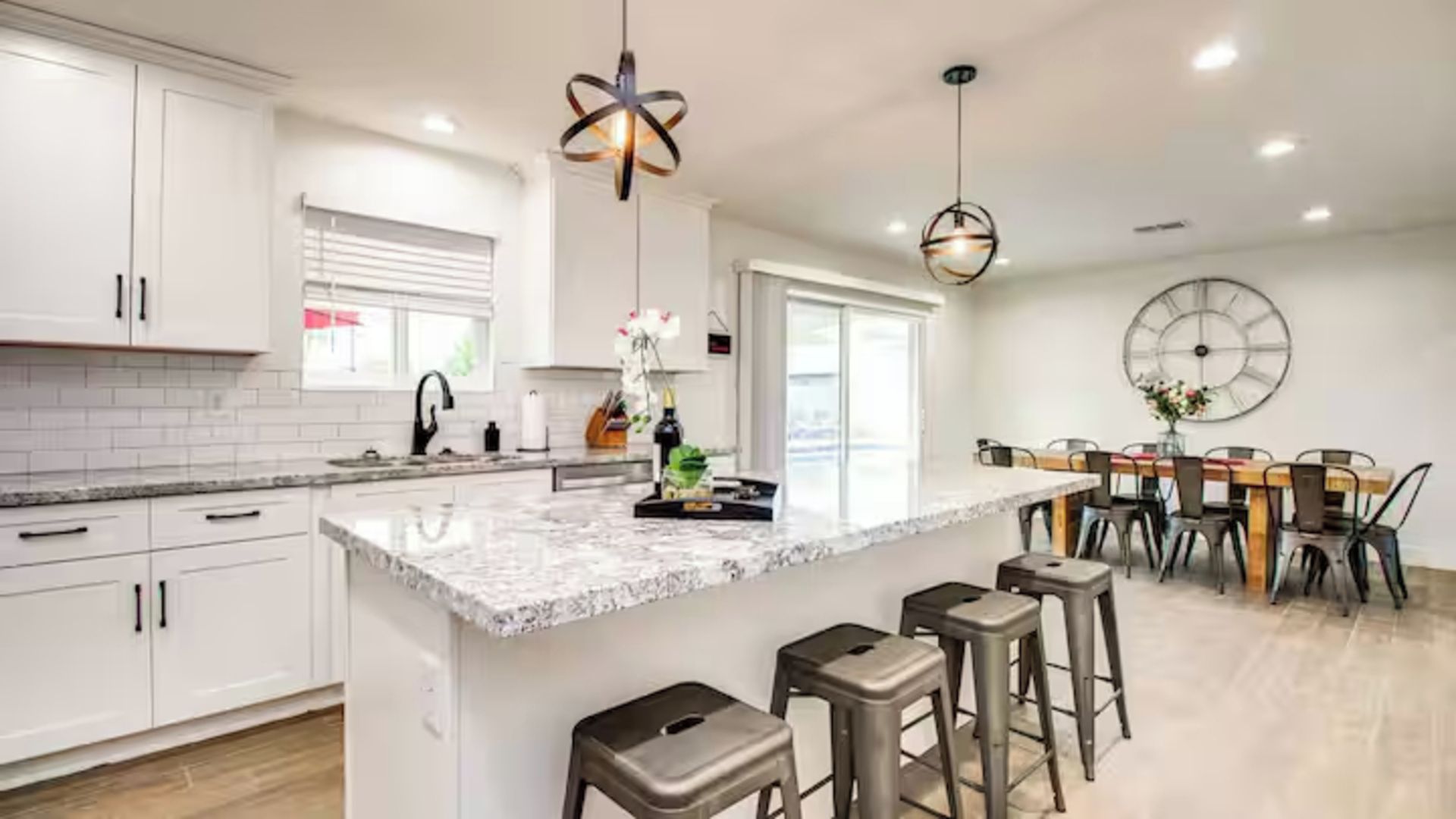 A modern kitchen with white cabinetry, a marble island, and bar stools.