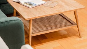 Un cuarto acogedor con un sofá verde, una mesa de centro de madera con una revista y dos copas de vino, y una ventana con cortinas de gasa.