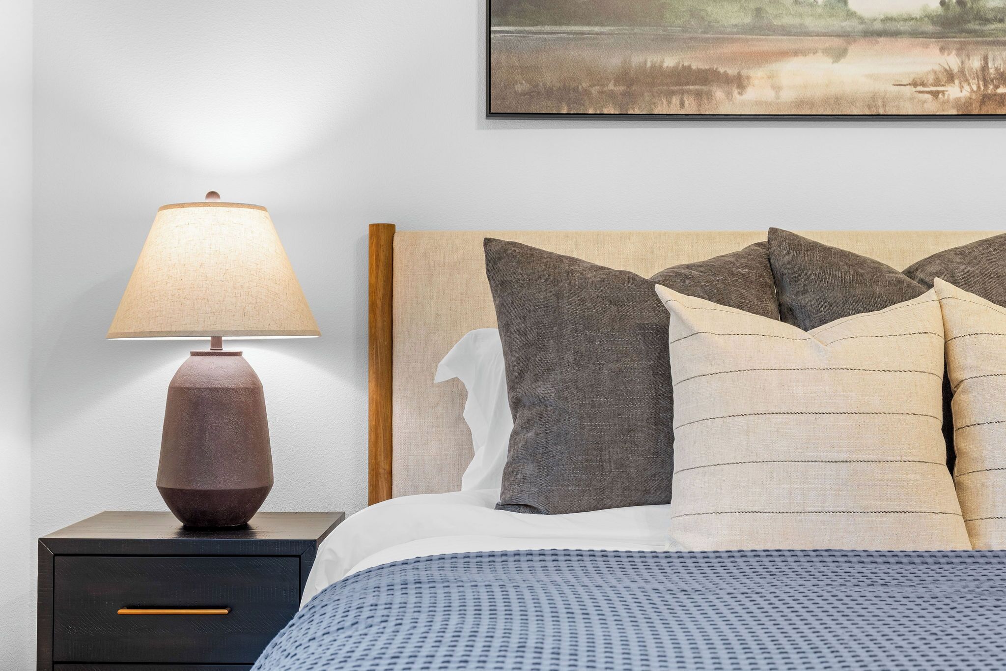 A neatly made bed with a patterned blue bedspread, a wooden nightstand with a lamp, and a framed picture on the wall.