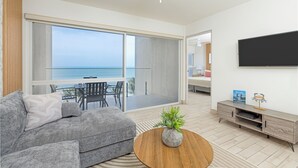 A modern living room with a grey sofa, a wooden coffee table, and a view of the ocean through large sliding doors.