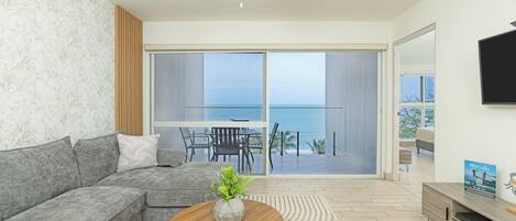 A modern living room with a grey sectional sofa, a wooden coffee table with a plant, and a view of the ocean through large sliding doors.