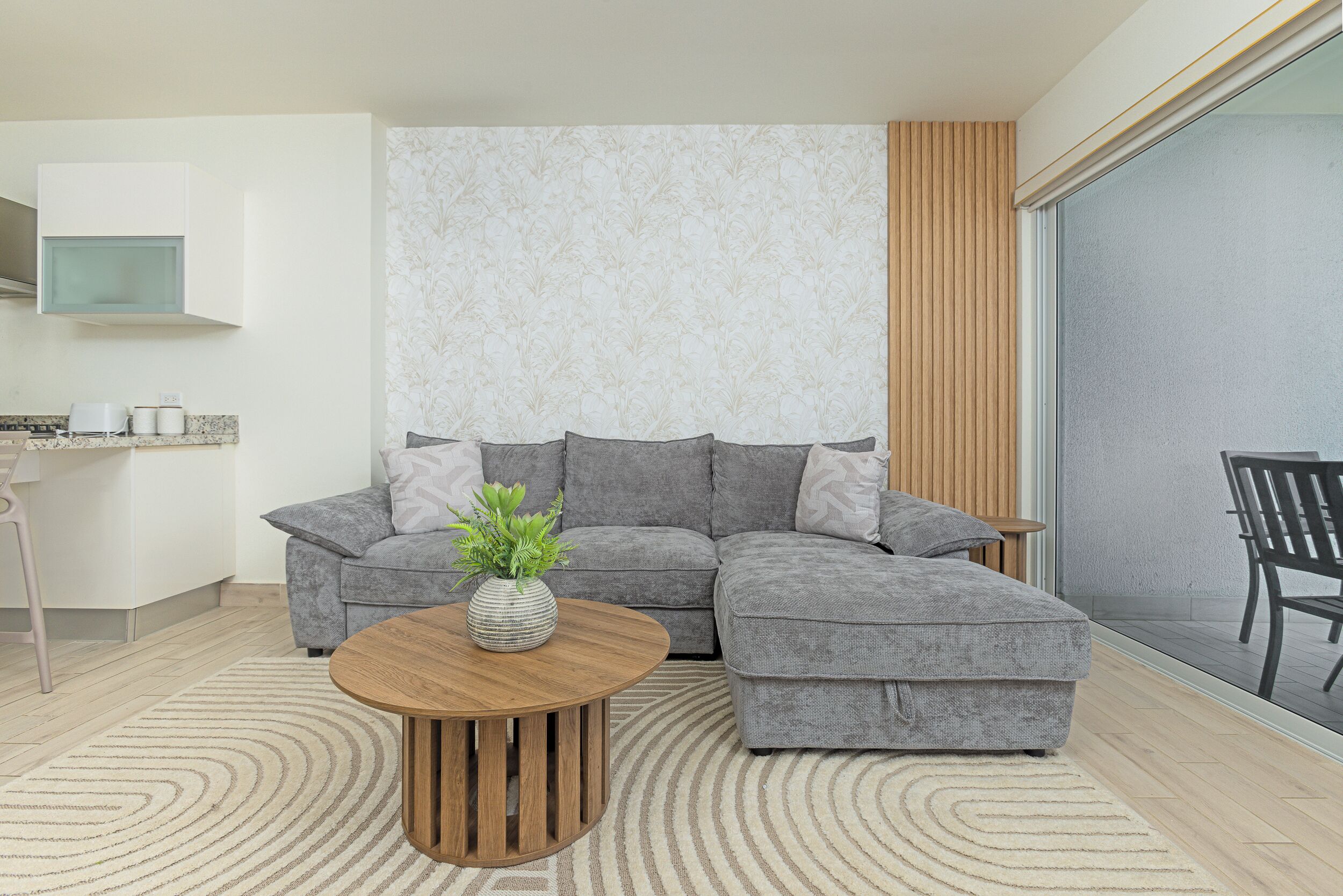 Een moderne woonkamer met een grijze modulaire bank, een houten salontafel en een groot raam met uitzicht.