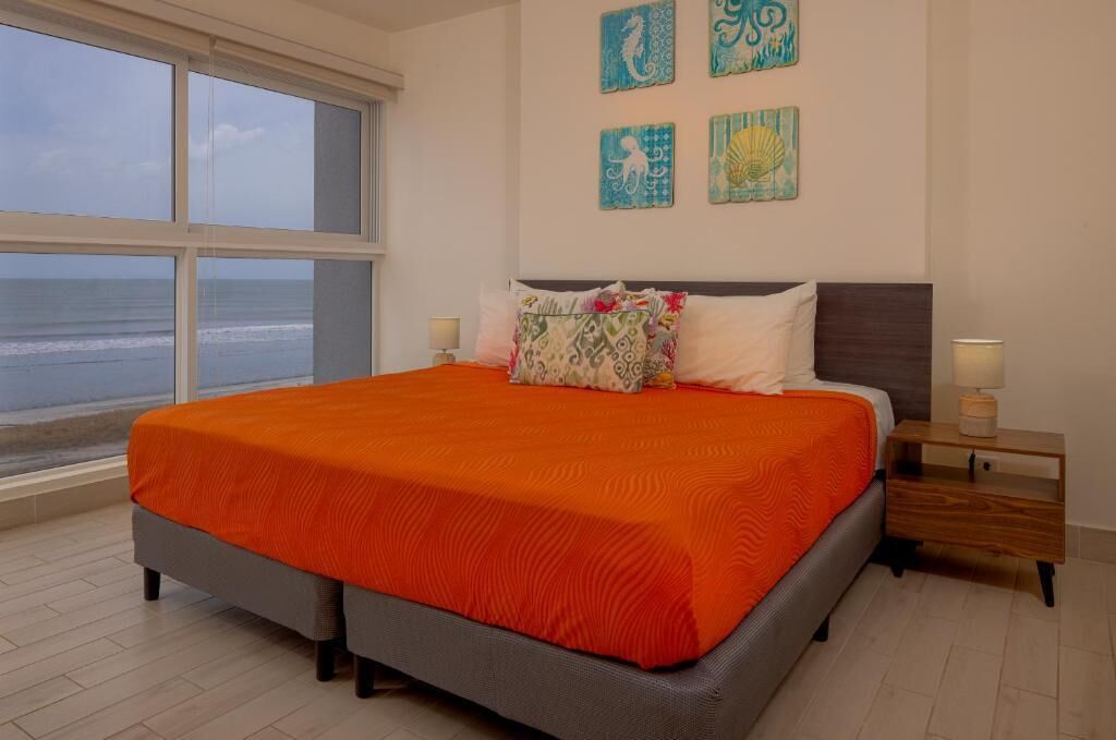 A bedroom with a large bed, a view of the ocean, and four wall art pieces.