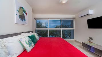 A bedroom with a large bed, a window with a view, a mounted TV, and an air conditioning unit.