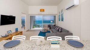 A modern living room with a large TV, seating area, and a view of the ocean.