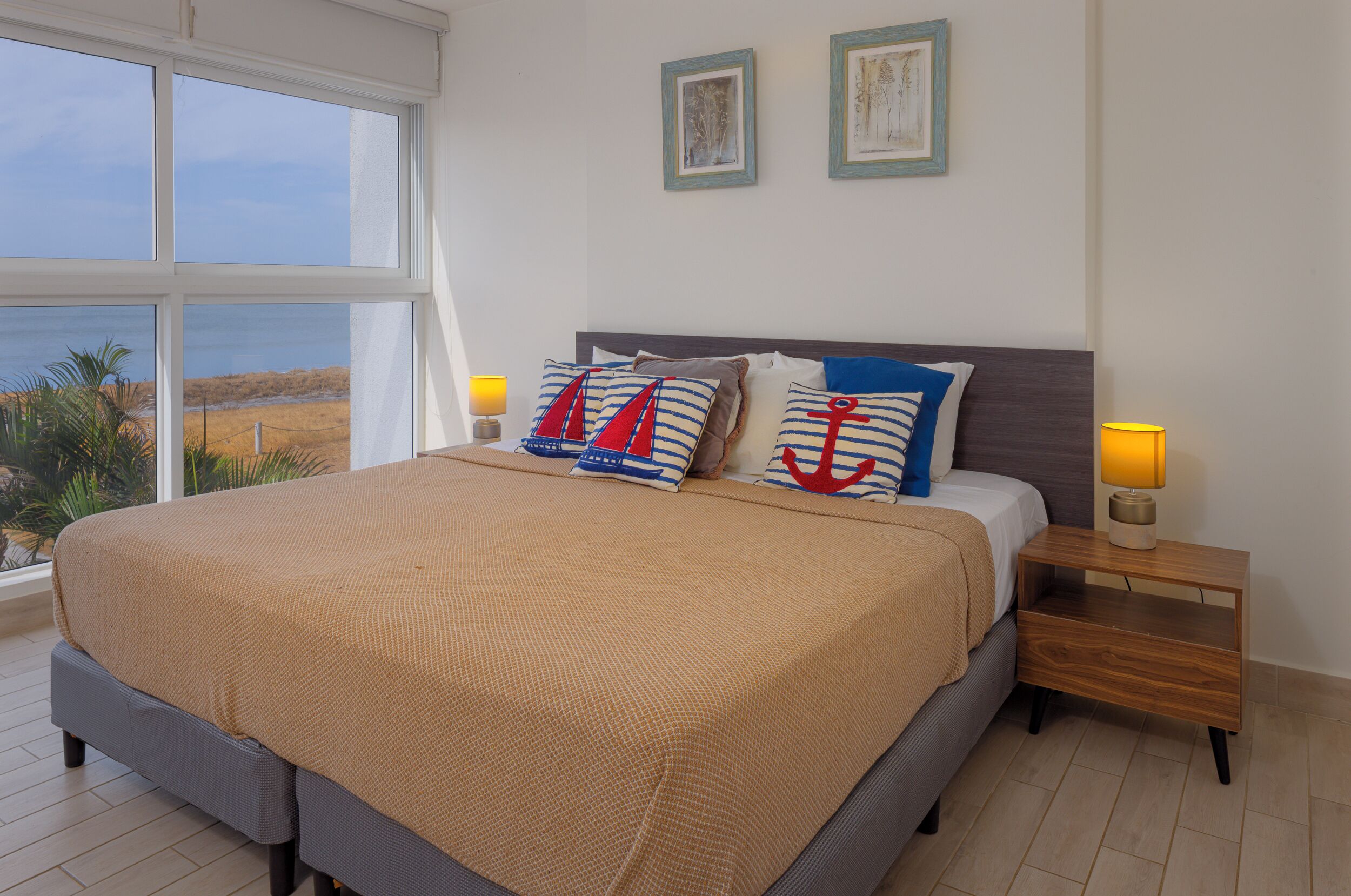 A bedroom with a large bed, two bedside tables, and a view of the beach.