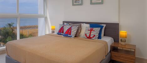 A bedroom with a large bed, two bedside tables, and a view of the beach.