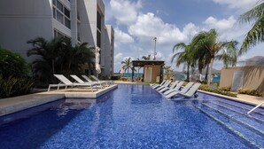 A swimming pool with lounge chairs, palm trees, and a building in the background.
