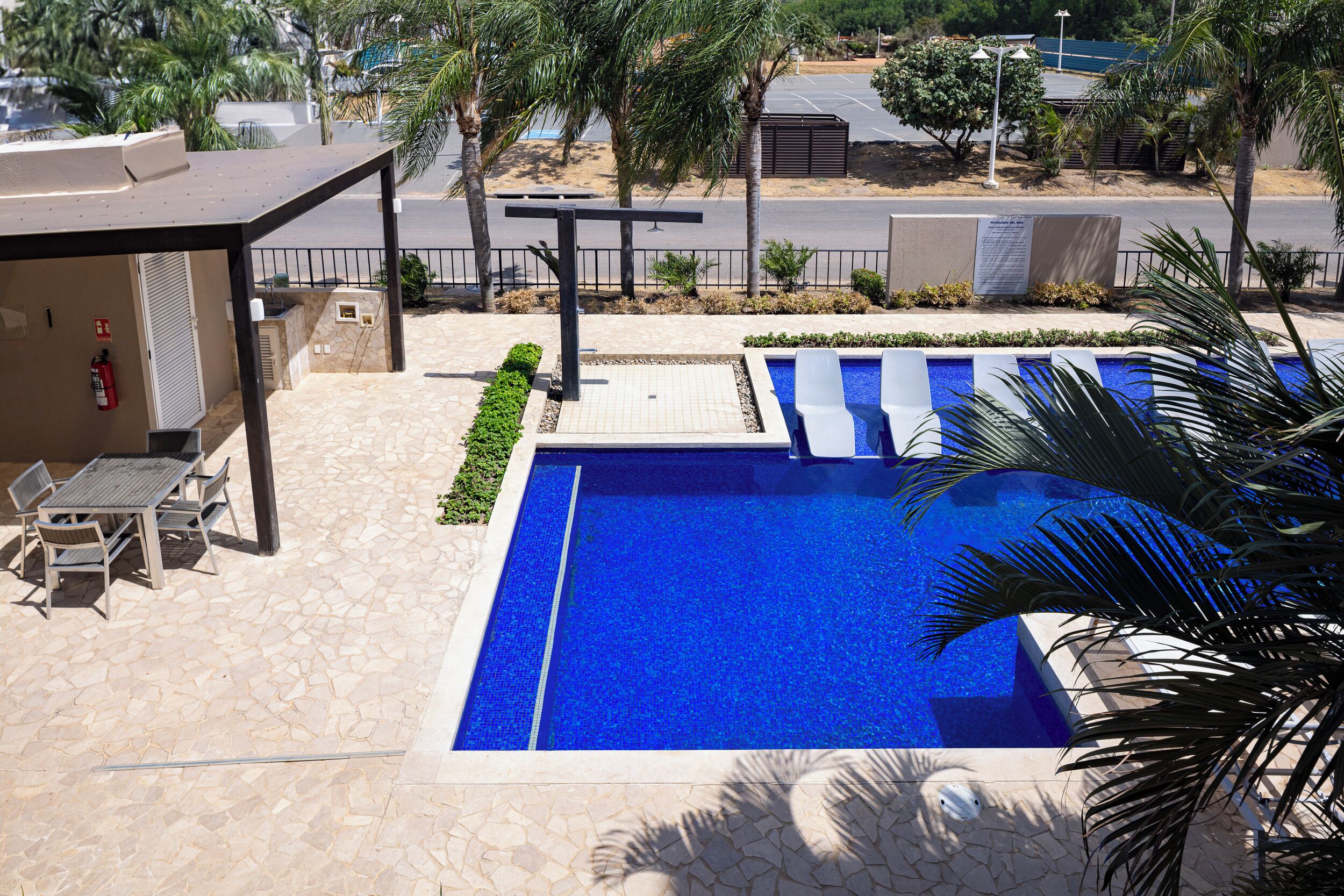 A swimming pool with a tiled deck, a covered seating area, and a view of the street.