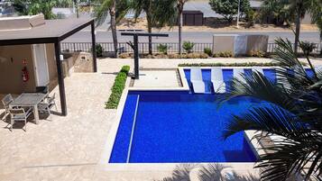 A swimming pool with a tiled deck, a covered seating area, and a view of the street.