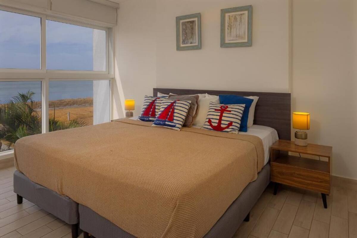 Een slaapkamer met een groot bed, twee bedlampen en uitzicht op het strand.