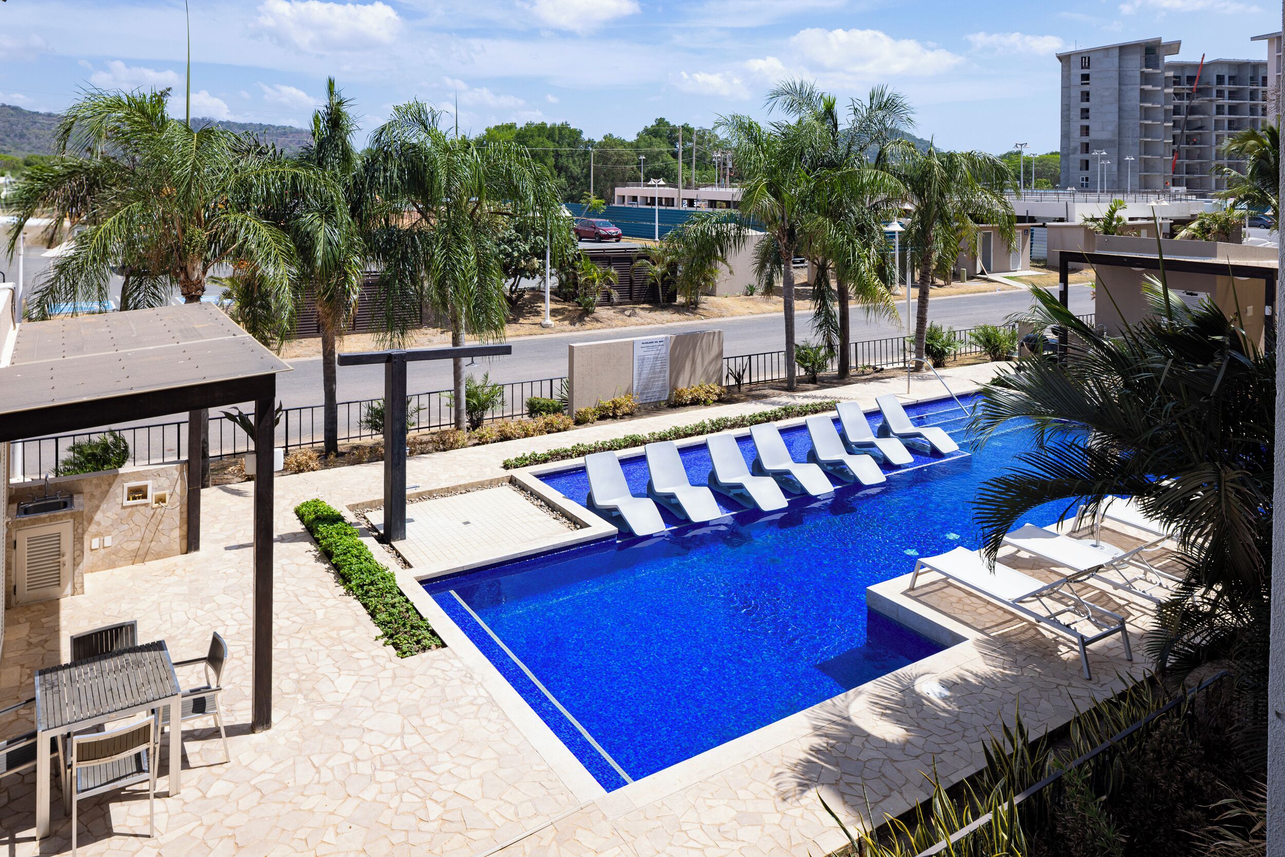 A swimming pool with lounge chairs, palm trees, and a stone patio.