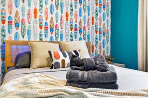 Un lit bien fait, avec une couverture à motifs, des oreillers et une serviette pliée.