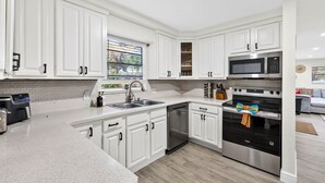 A modern kitchen with white cabinetry, stainless steel appliances, and a large window providing natural light. - Family Luxury Escape Heated Pool, Spa, Mini Golf, Arcade (Largo)