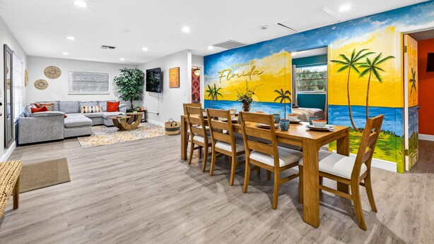 A modern living room with a dining area, featuring a large mural of Florida's sunset and palm trees. - Family Luxury Escape Heated Pool, Spa, Mini Golf, Arcade (Largo)