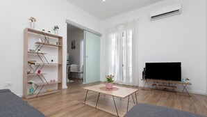 A modern living room with a wooden floor, a sofa, a coffee table, a TV, and a bookshelf. - Casa Belfiore Amacardo with Private Terrace (Giarre)