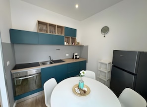 Una cocina moderna con armarios verde azulado, un lavamanos de acero inoxidable, un horno empotrado, un refrigerador negro y una mesa de comedor blanca con un jarrón.