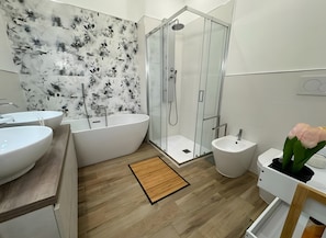 Un baño moderno con una bañera independiente, ducha con mampara de vidrio y lavamanos pedestal.