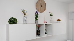 Un mur blanc orné d’une horloge en bois, d’une plante en pot, d’une bouteille et d’un petit bol, le tout posé sur une étagère blanche.