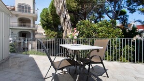 Une terrasse avec une table et des chaises, une balustrade et, au fond, un bâtiment doté d’un balcon.