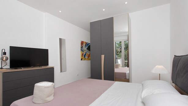 Une chambre à coucher moderne avec un lit, une table de chevet, une télévision et des œuvres d’art.