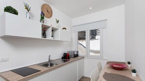 Une cuisine moderne avec des meubles blancs, un plan de travail en bois, un évier, une horloge et une fenêtre.