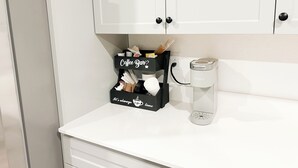 Une petite cuisine équipée d’un espace dédié à la préparation du café, comprenant une machine à café Keurig et une boîte de rangement pour le café, étiquetée « Coin café ».