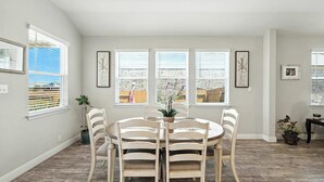 A dining area with a round table and six chairs, large windows with blinds, and framed artwork on the walls. - Shepherd’s Path | Pet-Friendly 3BR/2BA Monthly Rental in New Braunfels (New Braunfels)