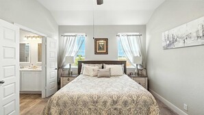 A bedroom with a large bed, two bedside tables with lamps, a nightstand, a window with curtains, and a painting on the wall. - Shepherd’s Path | Pet-Friendly 3BR/2BA Monthly Rental in New Braunfels (New Braunfels)
