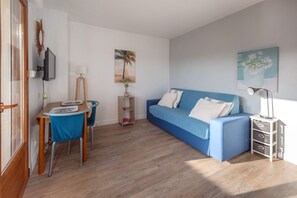 A living room with a blue sofa, a wooden coffee table, a TV mounted on the wall, and a small side table with a lamp. - Le Fabre Azur - 600 m de la plage, parking (Saint-Aygulf)