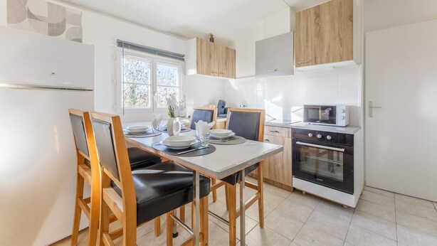 A modern kitchen with a dining table, chairs, a refrigerator, an oven, and cabinets. - Du côté de Giverny - Avec Parking Privé (Bennecourt)