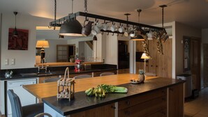 A modern kitchen with a central island, wooden cabinets, and hanging pots. - Le Gite de Caroline - Avec Parking Privé (Fère-en-Tardenois)