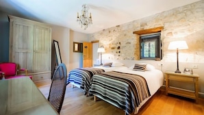 A bedroom with two beds, a wooden wardrobe, a dining table, and a stone wall. - Le Gite de Caroline - Avec Parking Privé (Fère-en-Tardenois)