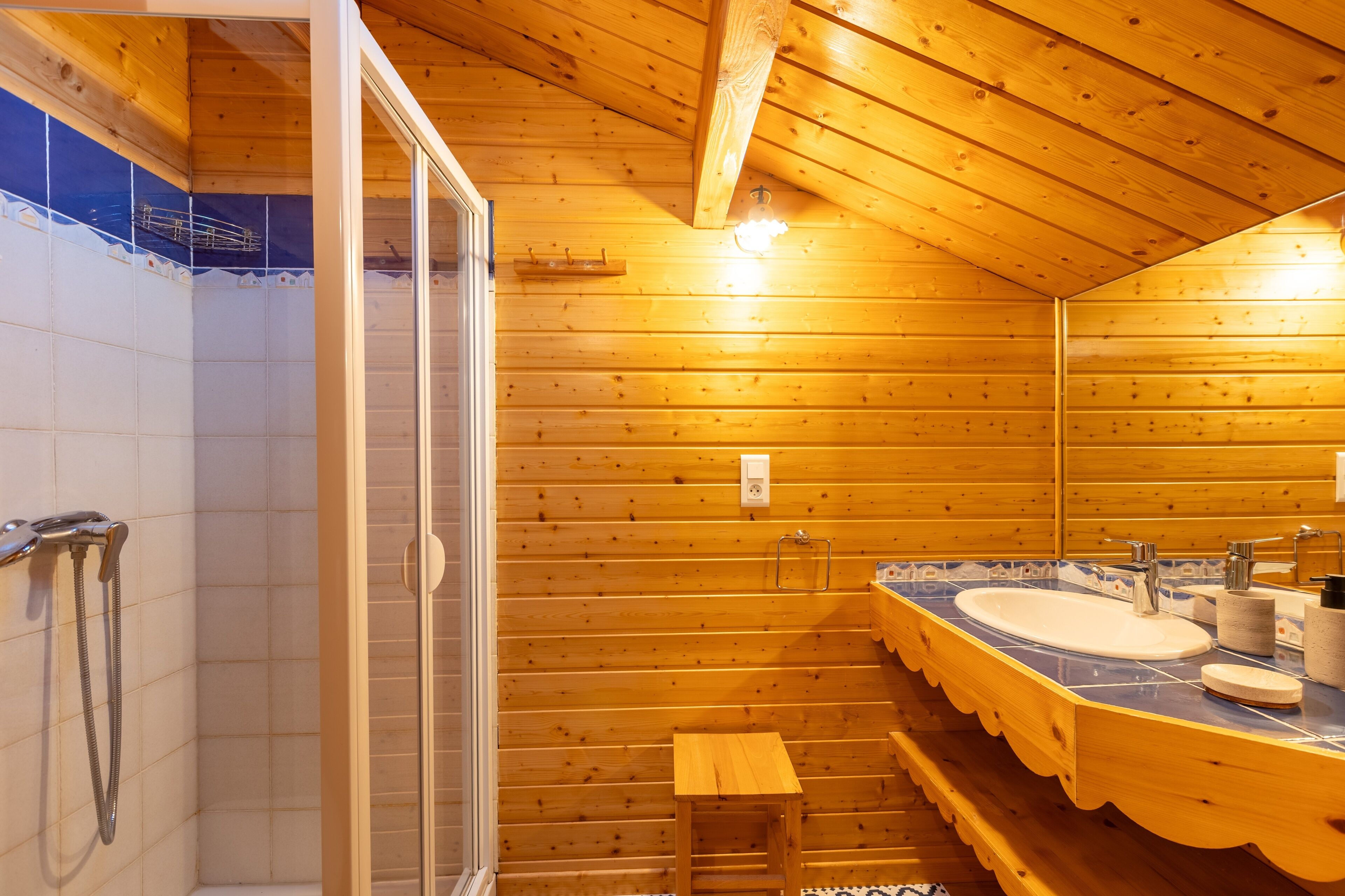 Une salle de bain rustique, aménagée dans une cabane en bois, avec une douche, un lavabo et un petit tabouret en bois.
