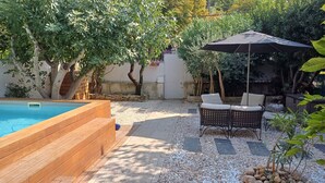 A backyard with a swimming pool, a wooden deck, and outdoor furniture under a large umbrella. - Soleil Provençal - Avec piscine privée (Avignon)