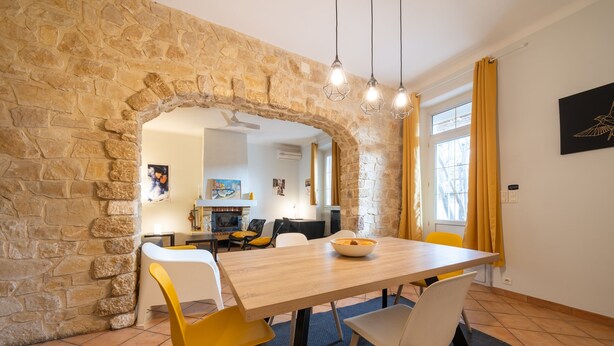 A dining area with a stone archway, a wooden table, and yellow and white chairs. - Soleil Provençal - Avec piscine privée (Avignon)