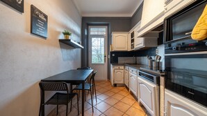 A compact kitchen with white cabinets, a black countertop, and a built-in oven. There is a small window above the sink and a potted plant on the countertop. - Soleil Provençal - Avec piscine privée (Avignon)