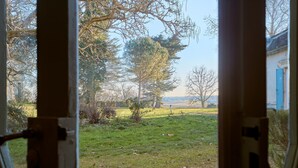 A view through a window with a wooden frame, revealing a grassy outdoor area with trees and a distant building. - Château Tour Chapoux - Piscine privée (Saint-Antoine-du-Queyret)