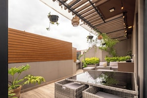 Eine moderne Außenpatio mit Korbmöbeln, hängenden Pflanzgefäßen und einem Tisch mit Glasplatte.